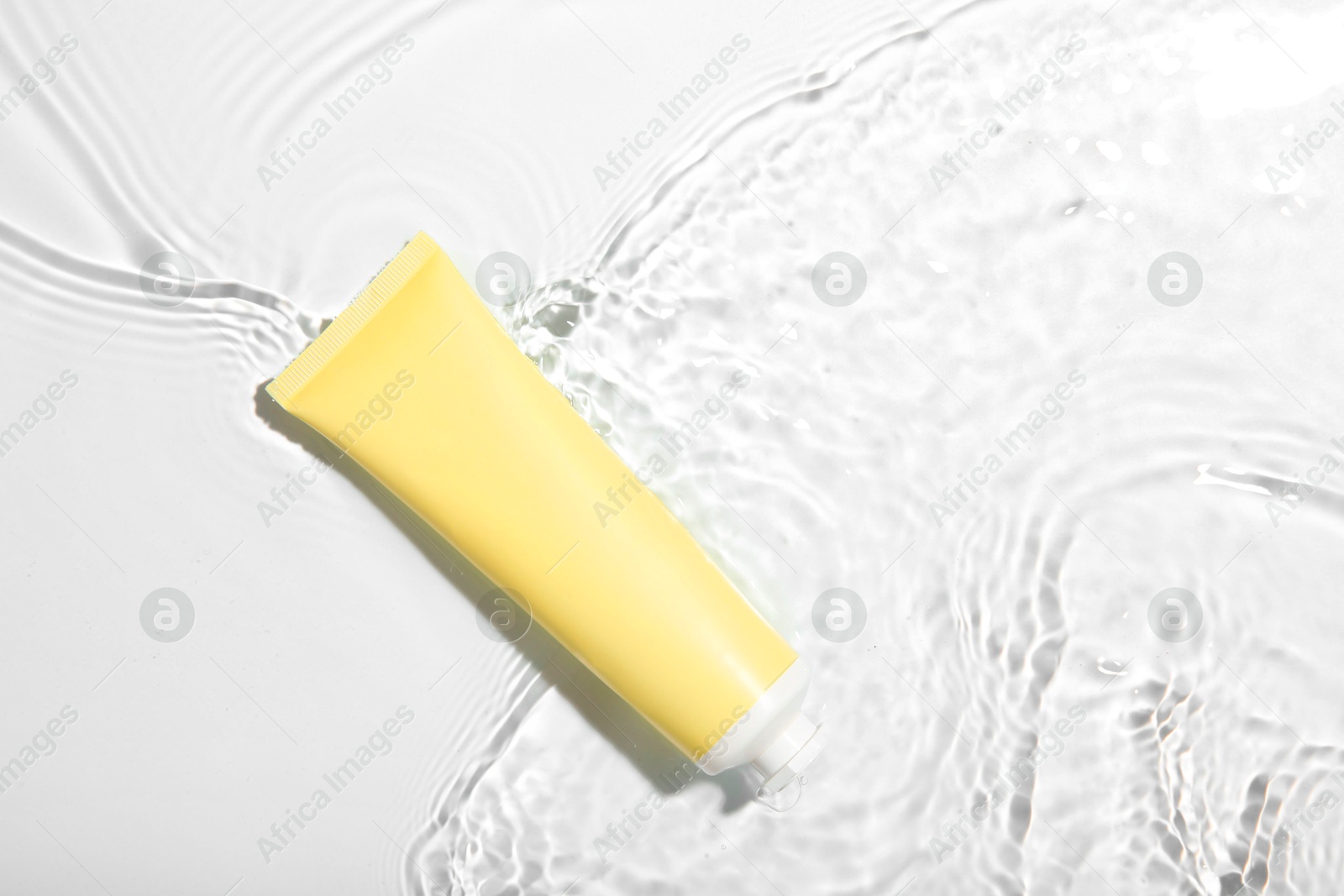 Photo of Cosmetic product. Tube with cream in water on light background, top view