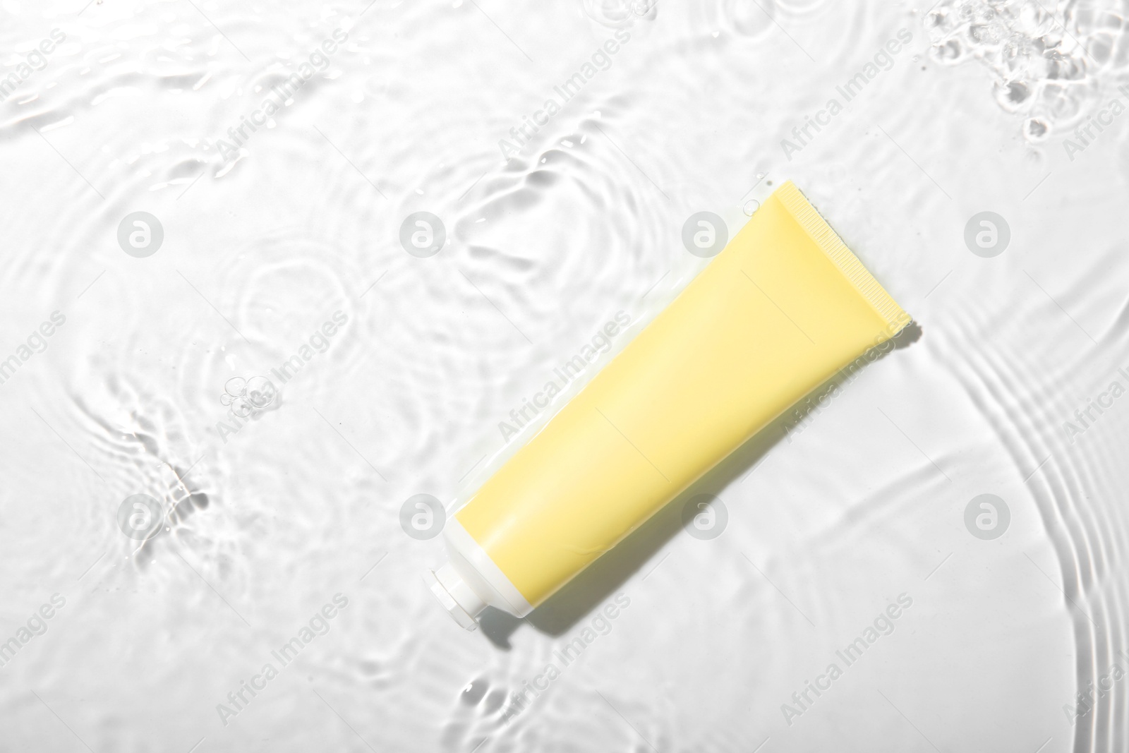 Photo of Cosmetic product. Tube with cream in water on light background, top view