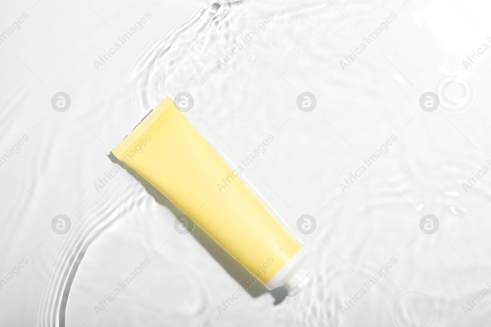 Photo of Cosmetic product. Tube with cream in water on light background, top view