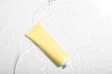 Photo of Cosmetic product. Tube with cream in water on light background, top view