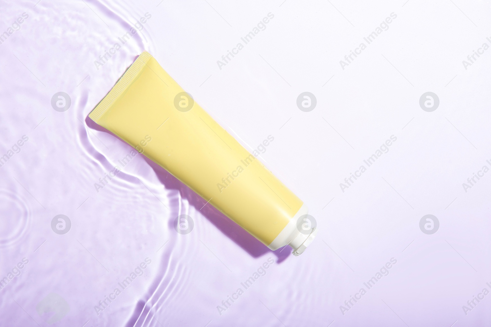 Photo of Cosmetic product. Tube with cream in water on light background, top view