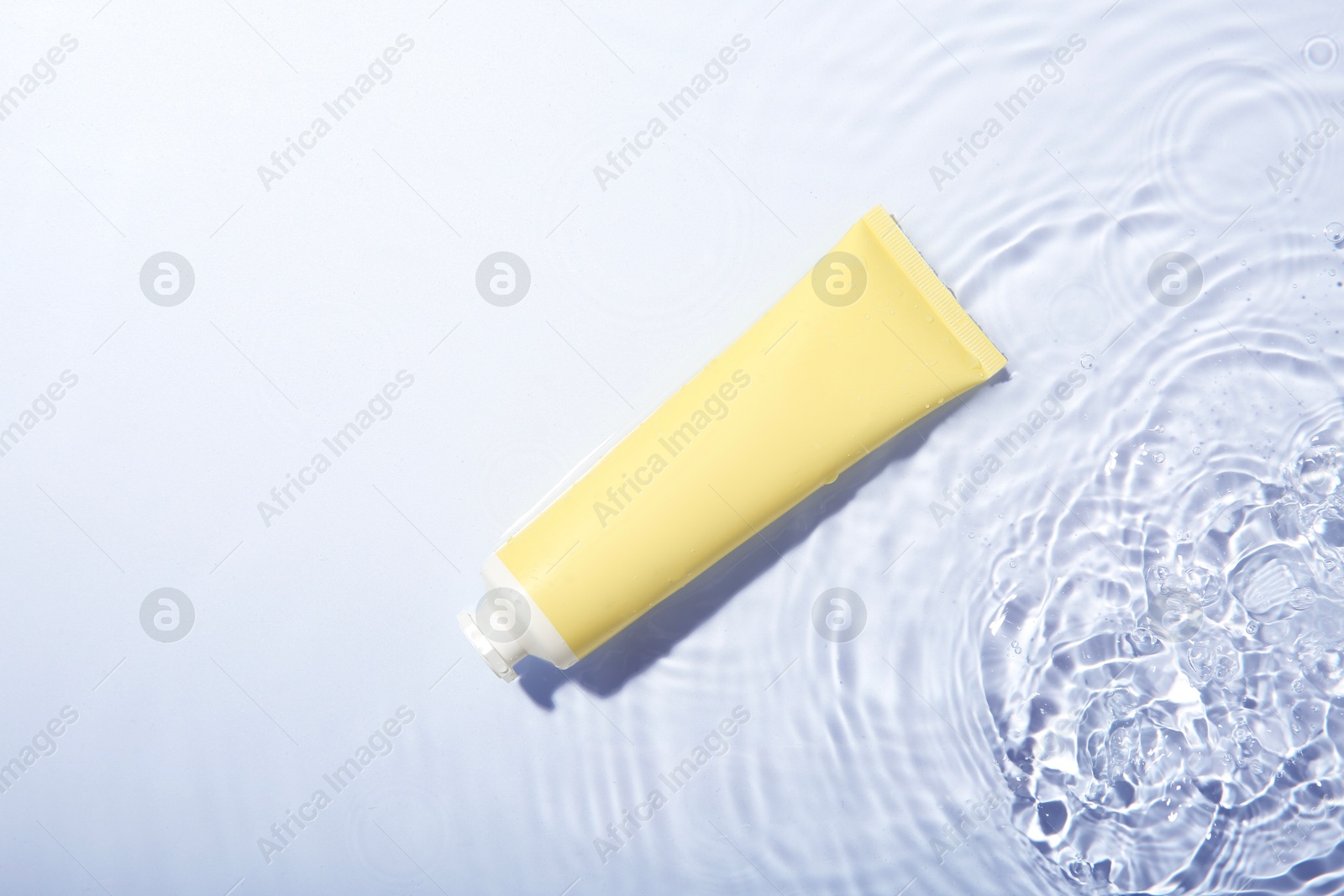 Photo of Cosmetic product. Tube with cream in water on light background, top view