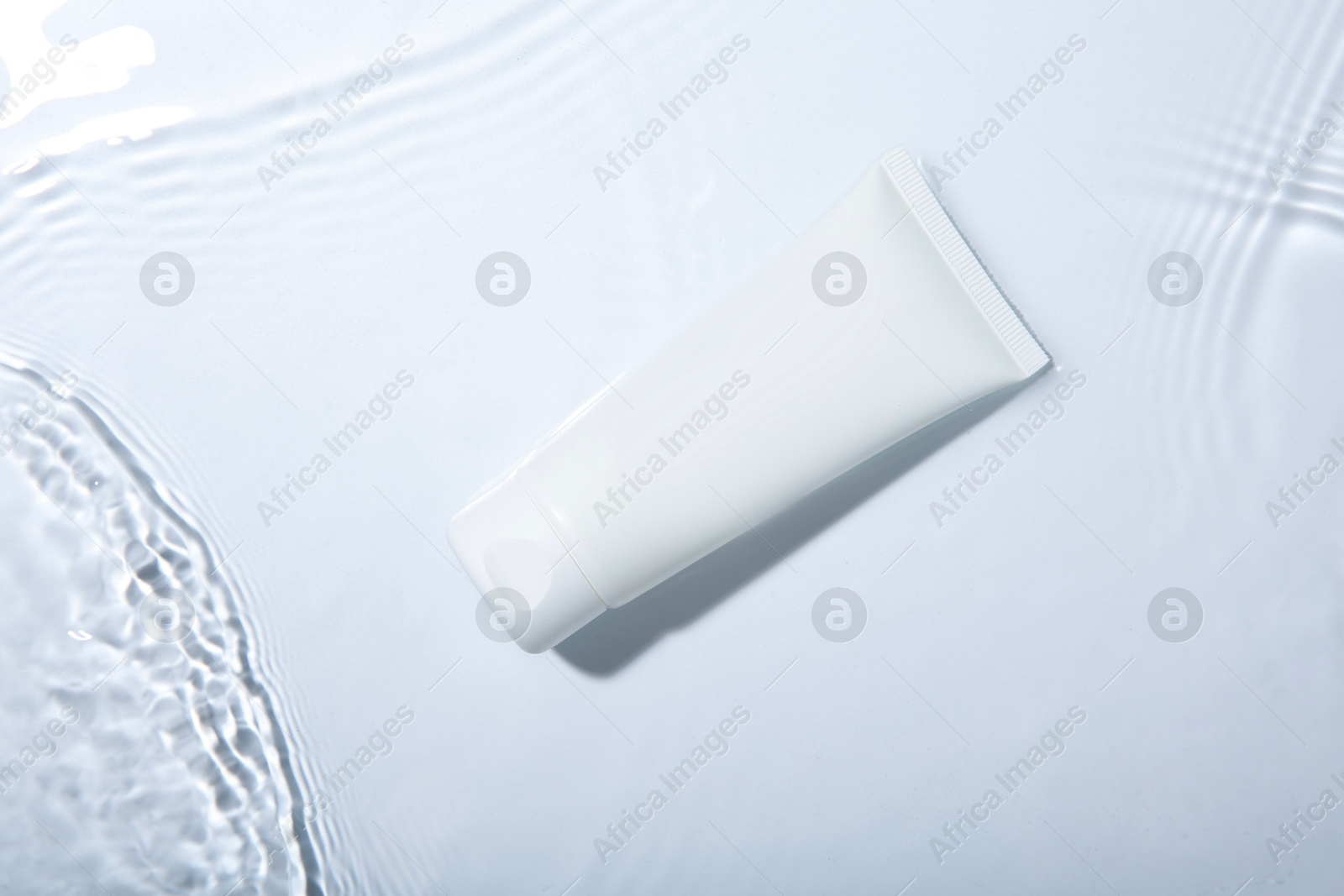 Photo of Cosmetic product. Tube with cream in water on light background, top view