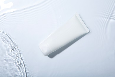 Cosmetic product. Tube with cream in water on light background, top view