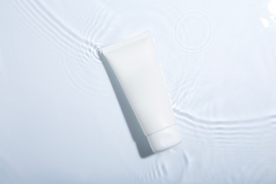 Cosmetic product. Tube with cream in water on light background, top view