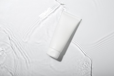 Photo of Cosmetic product. Tube with cream in water on light background, top view