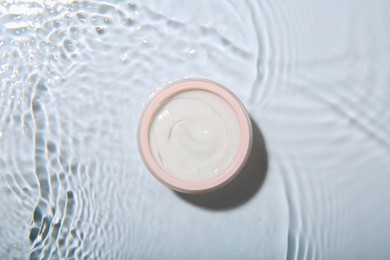 Photo of Cosmetic product. Jar with cream in water on light background, top view