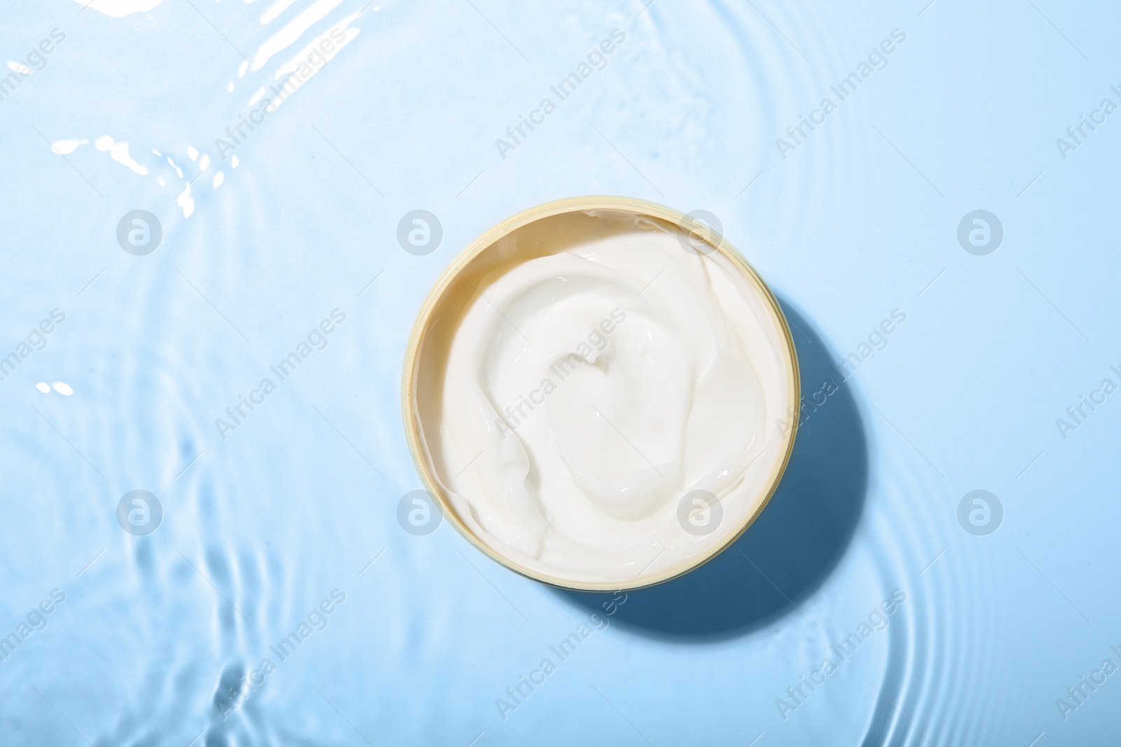 Photo of Cosmetic product. Jar with cream in water on light background, top view