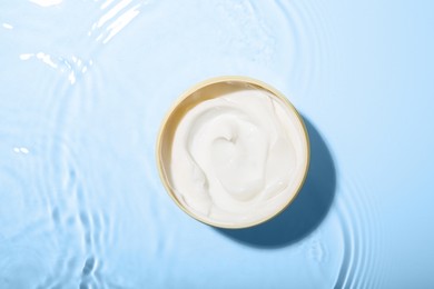 Photo of Cosmetic product. Jar with cream in water on light background, top view