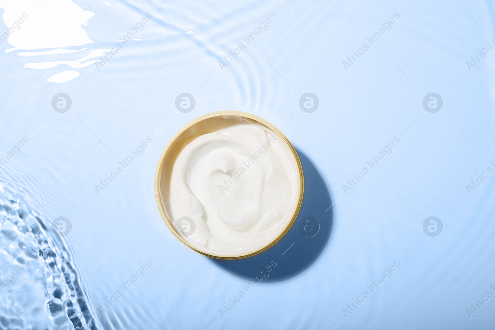 Photo of Cosmetic product. Jar with cream in water on light background, top view