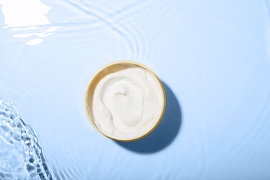 Photo of Cosmetic product. Jar with cream in water on light background, top view