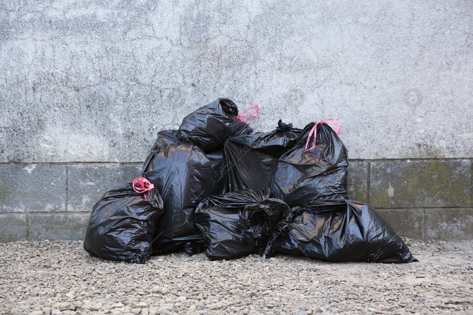 Photo of Many trash bags with garbage near wall outdoors