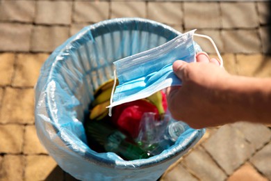 Photo of Man throwing medical mask into garbage bin outdoors, closeup