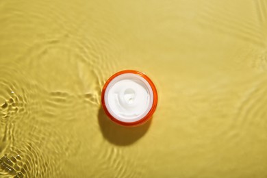 Photo of Jar with cream in water on yellow background, top view. Cosmetic product