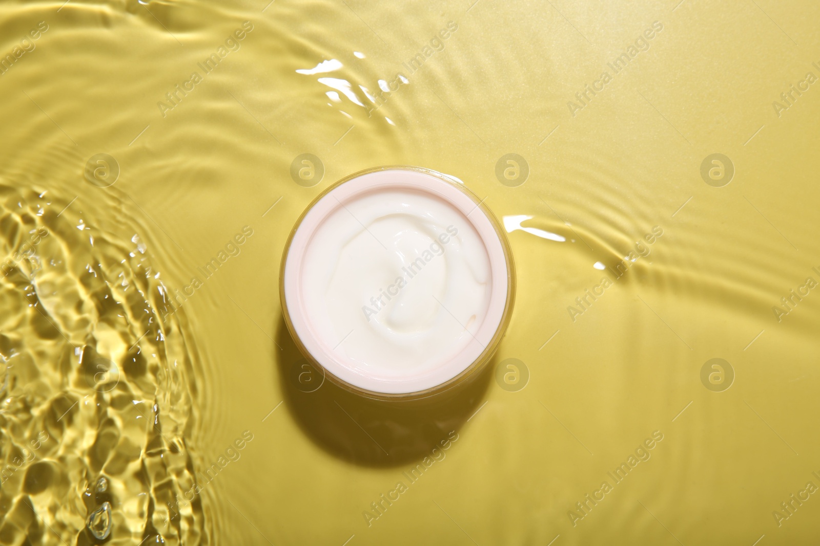 Photo of Jar with cream in water on yellow background, top view. Cosmetic product