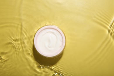 Photo of Cosmetic product. Jar with cream in water on yellow background, top view. Space for text