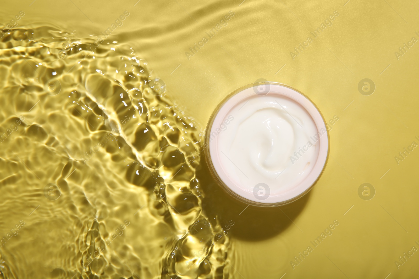 Photo of Jar with cream in water on yellow background, top view. Cosmetic product