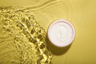 Photo of Jar with cream in water on yellow background, top view. Cosmetic product