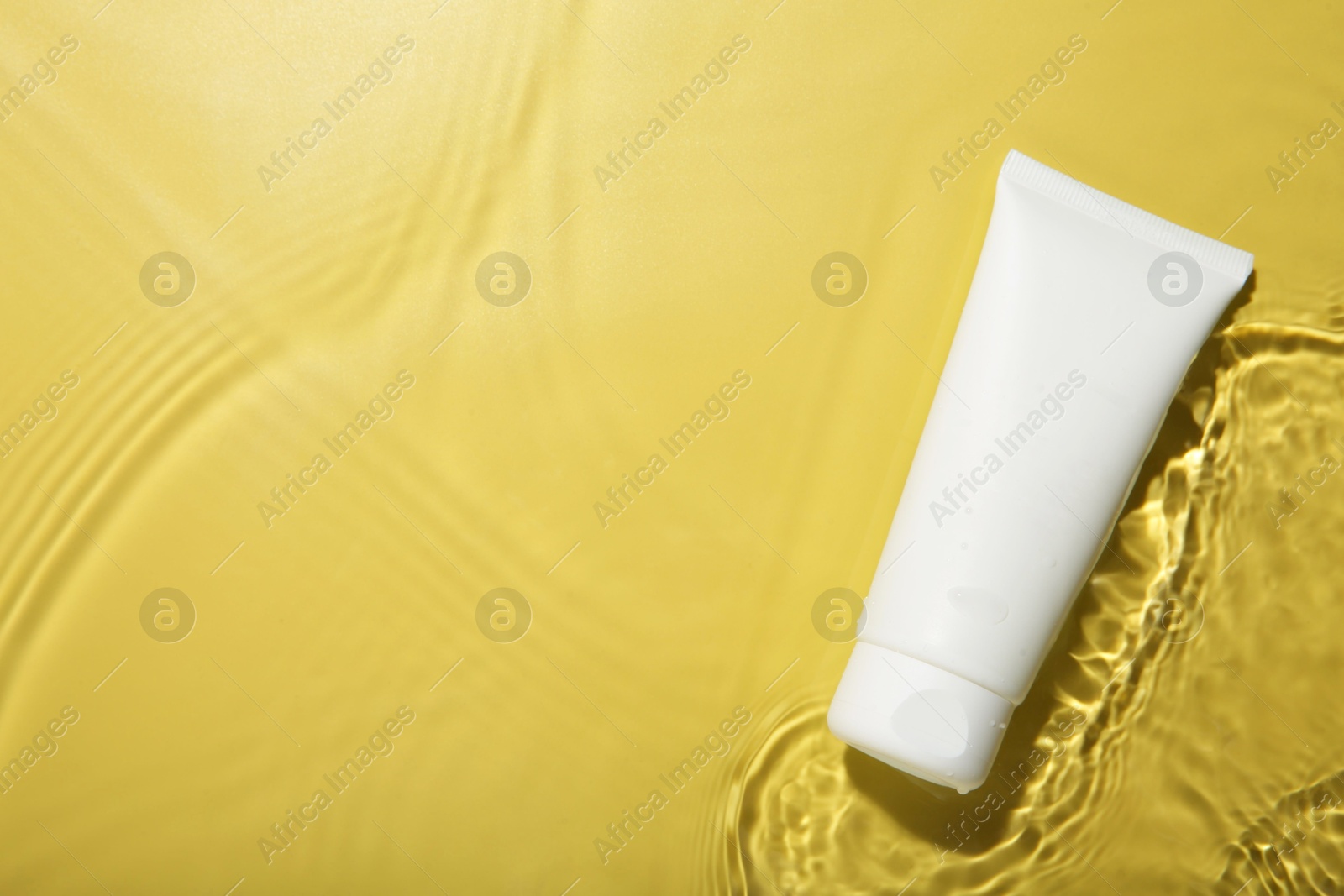 Photo of Cosmetic product. Tube with cream in water on yellow background, top view. Space for text