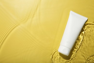 Cosmetic product. Tube with cream in water on yellow background, top view. Space for text