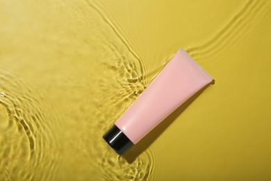 Tube with cream in water on yellow background, top view. Cosmetic product