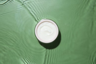 Jar with cream in water on light green background, top view. Cosmetic product