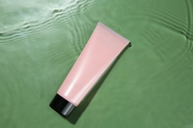 Photo of Tube with cream in water on light green background, top view. Cosmetic product