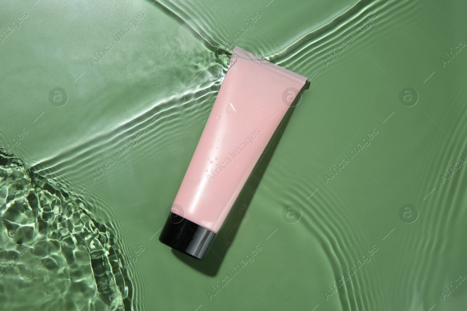 Photo of Tube with cream in water on light green background, top view. Cosmetic product