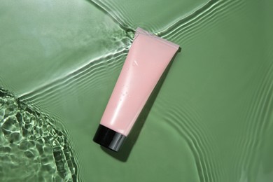 Photo of Tube with cream in water on light green background, top view. Cosmetic product