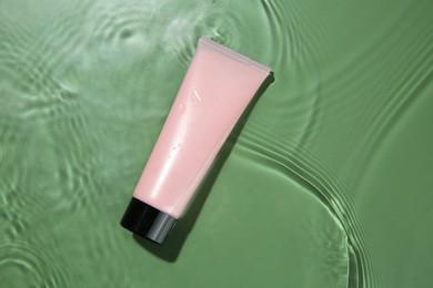 Photo of Tube with cream in water on light green background, top view. Cosmetic product