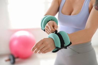 Woman putting ankle weight on her arm indoors, closeup