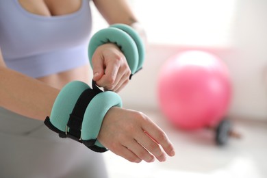 Photo of Woman putting ankle weight on her arm indoors, closeup