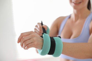 Woman putting ankle weight on her arm indoors, closeup