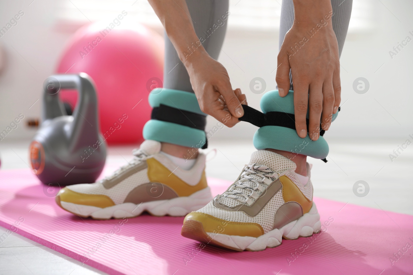 Photo of Woman putting on ankle weights indoors, closeup