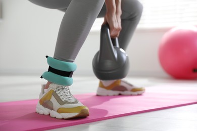 Photo of Woman with ankle weights and kettlebell training indoors, closeup