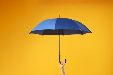 Woman with blue umbrella on yellow background, closeup