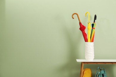 Photo of Colorful umbrellas in holder and backpacks near green wall, space for text