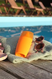 Photo of Stylish sunglasses, towel and sunscreen near outdoor swimming pool