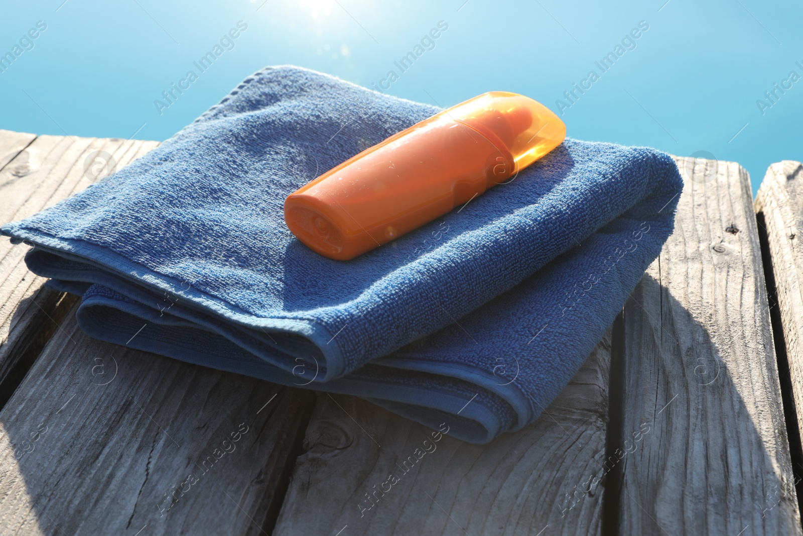 Photo of Stylish sunglasses, towel and sunscreen on wooden deck near outdoor swimming pool