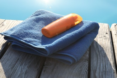 Photo of Stylish sunglasses, towel and sunscreen on wooden deck near outdoor swimming pool