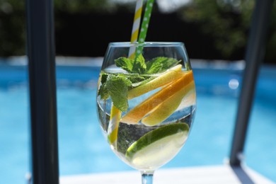 Photo of Tasty cocktail in glass near swimming pool outdoors