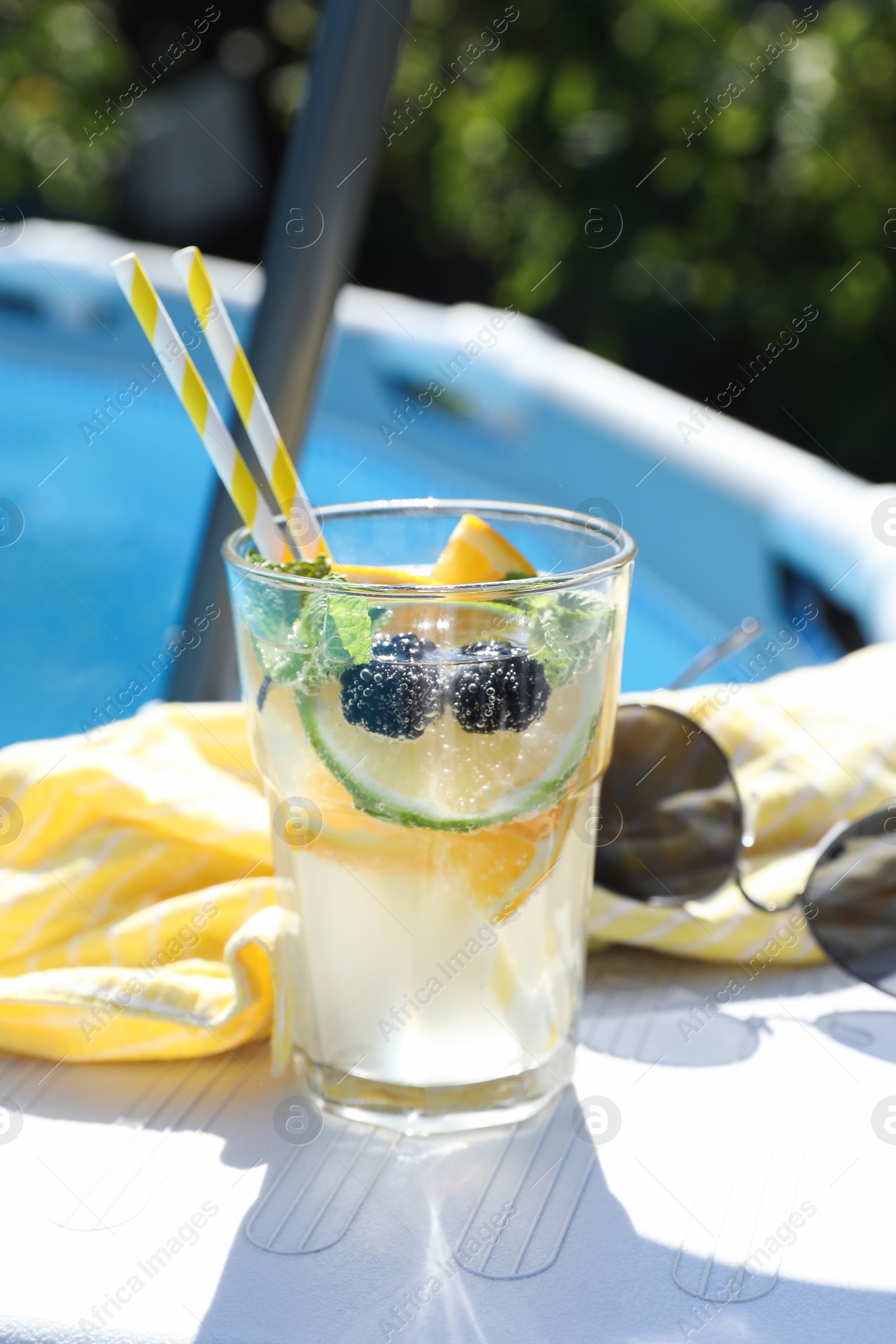 Photo of Tasty cocktail in glass and sunglasses near swimming pool outdoors