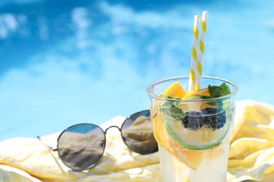 Tasty cocktail in glass and sunglasses near swimming pool outdoors, closeup