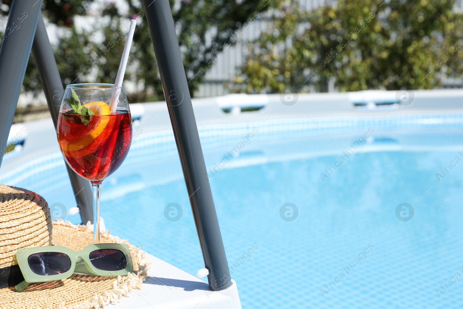 Photo of Tasty cocktail in glass and sunglasses near swimming pool outdoors