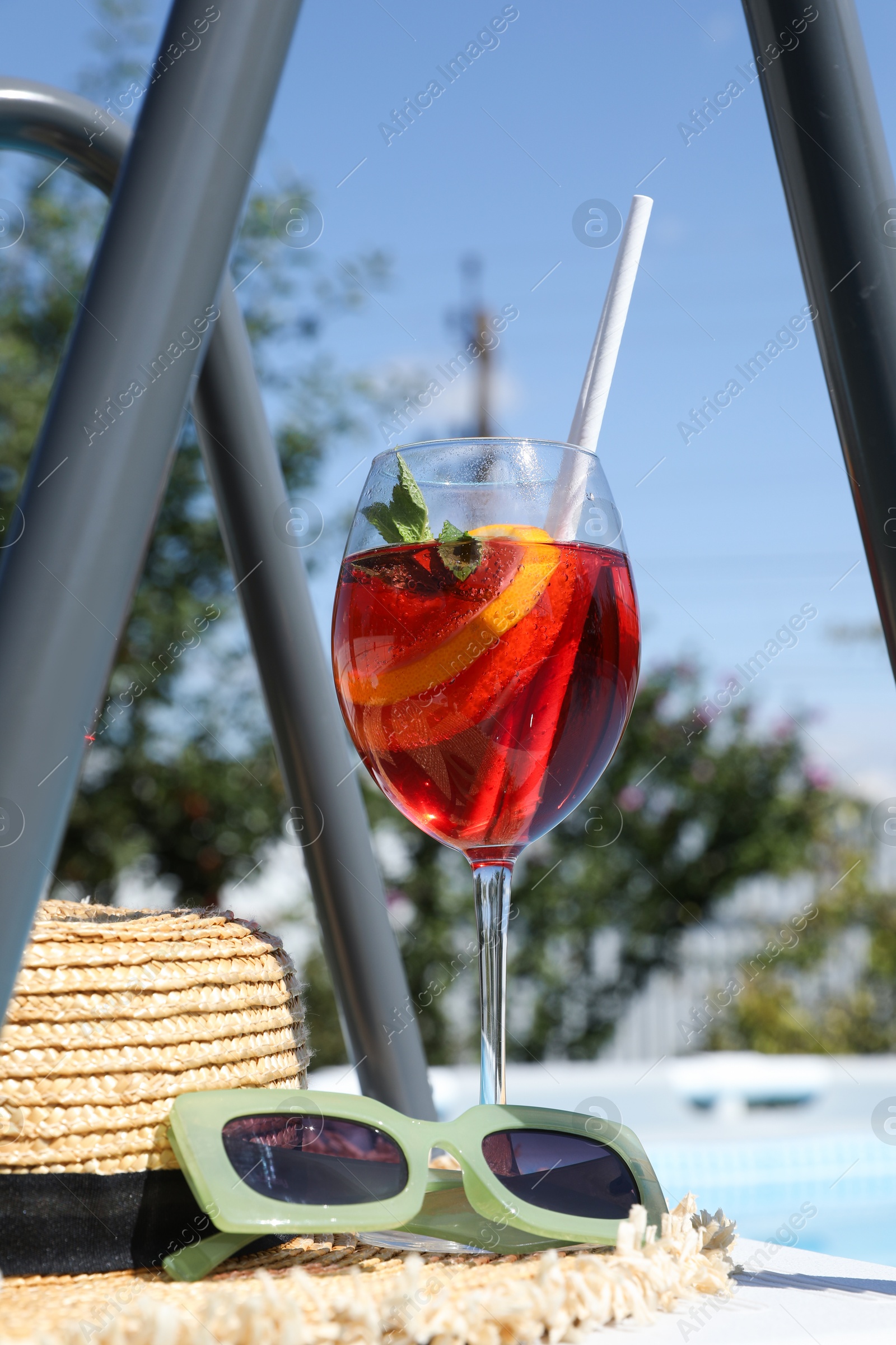 Photo of Tasty cocktail in glass and sunglasses near swimming pool outdoors