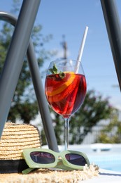 Tasty cocktail in glass and sunglasses near swimming pool outdoors