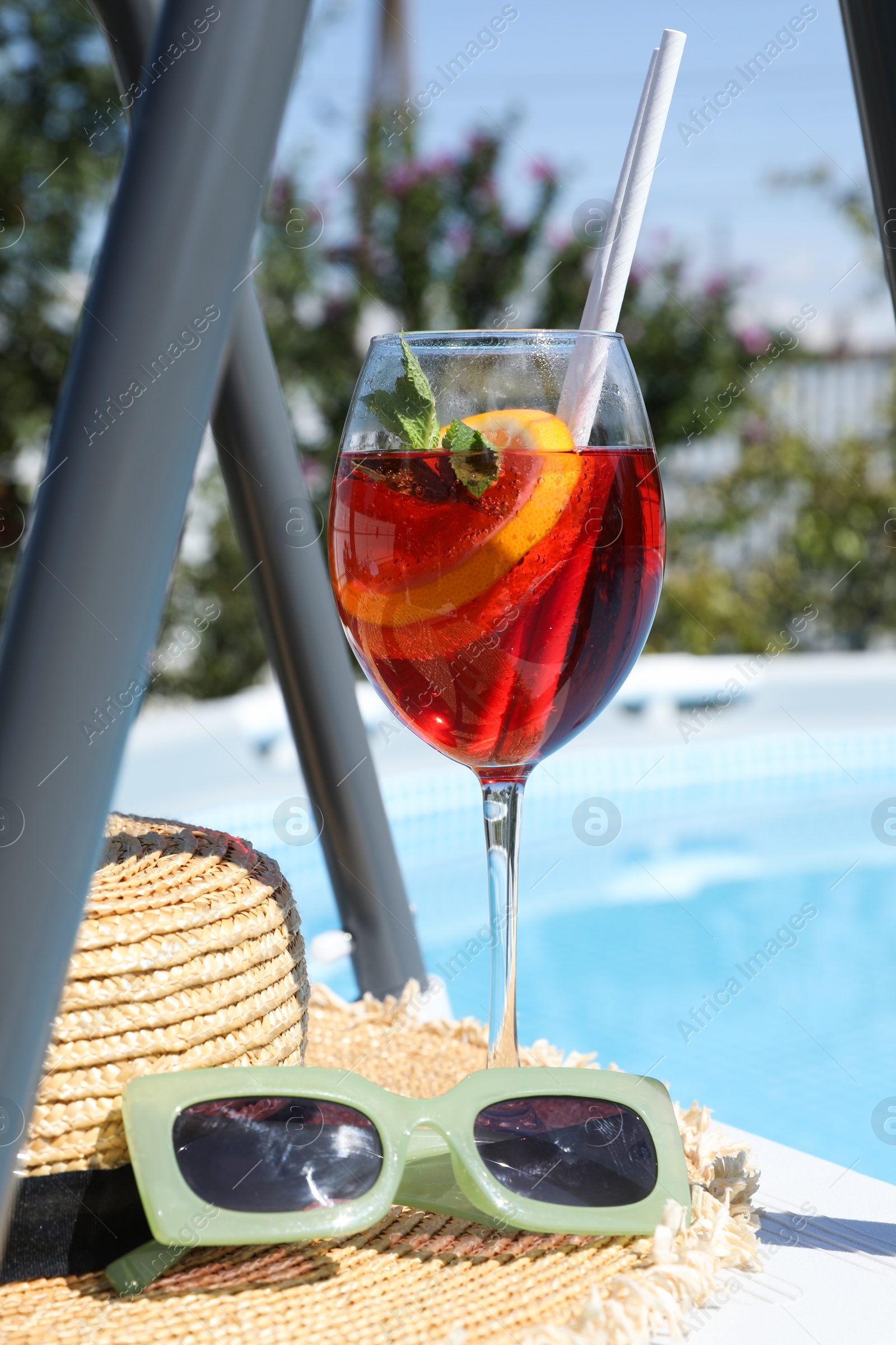 Photo of Tasty cocktail in glass and sunglasses near swimming pool outdoors