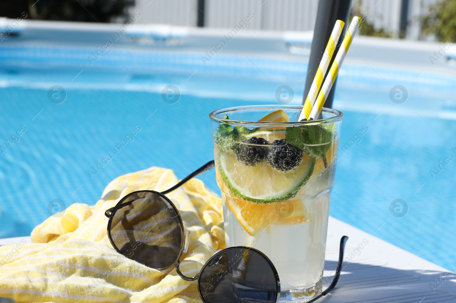 Photo of Tasty cocktail in glass and sunglasses near swimming pool outdoors