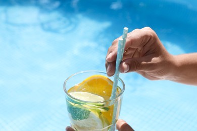 Photo of Woman holding tasty cocktail in glass near swimming pool outdoors, closeup