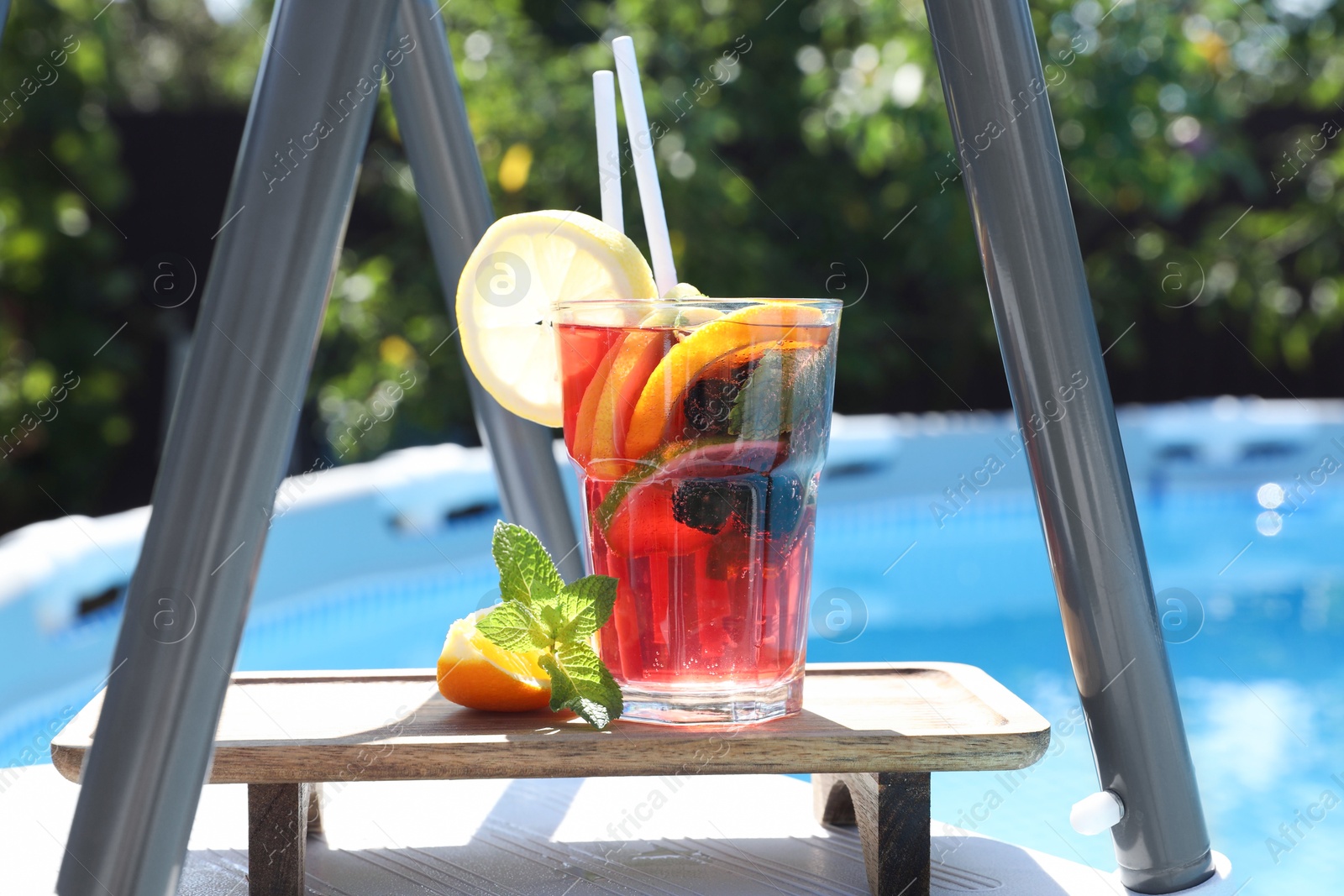 Photo of Tasty cocktail in glass near swimming pool outdoors